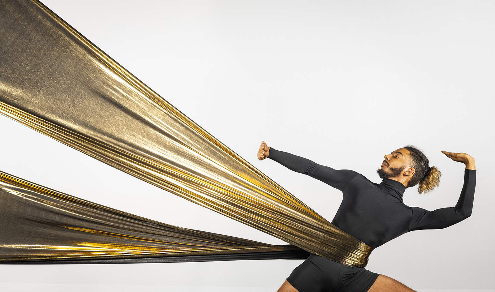 Dancer stretches gold fabric as he leans to the right