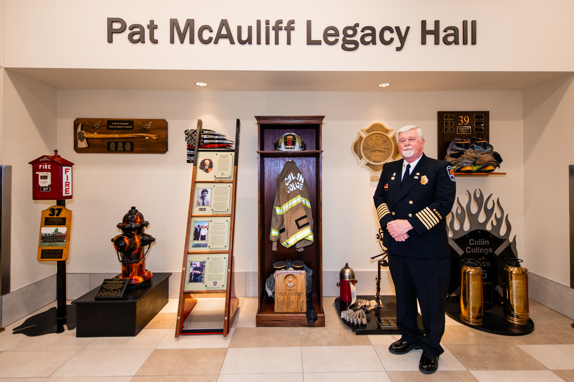 Man in uniform stands in front of memorabilia wall. 